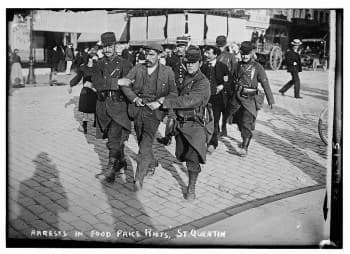 A vintage image of officers walking a man in handcuffs away in a large group.