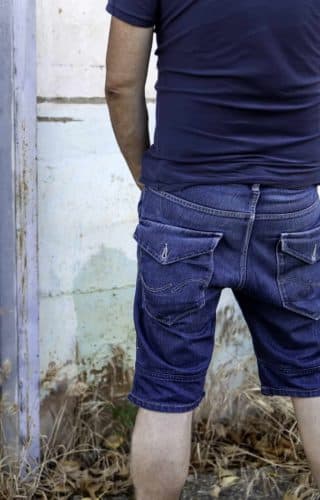 a man urinating in public against a white wall